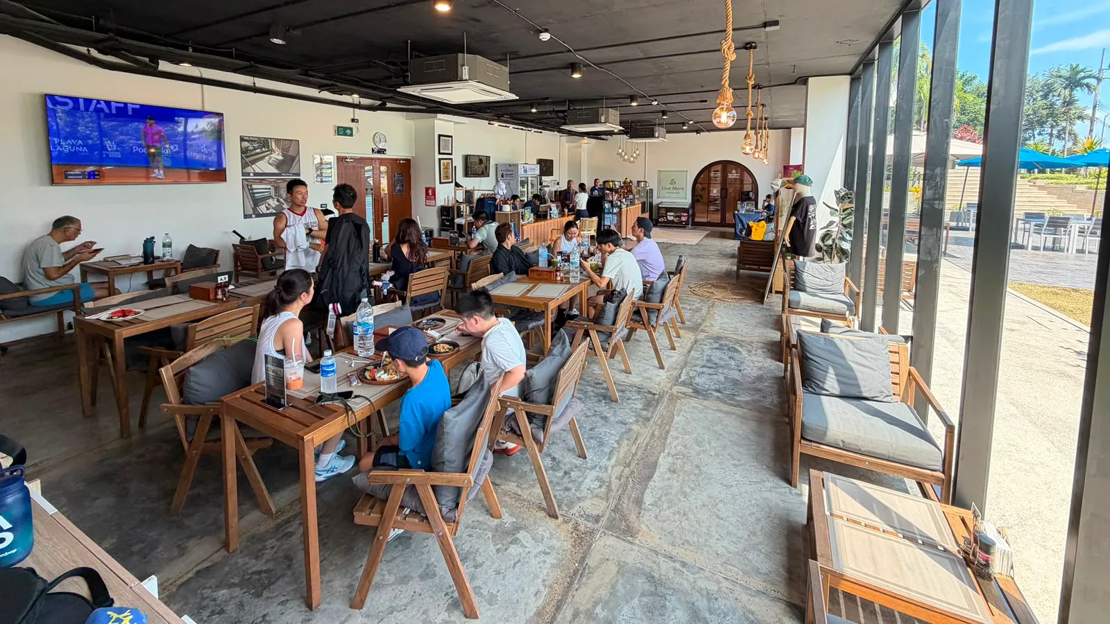 Guests dining at the Courtside Café at KĀHLĪ Phuket, the room opening onto the terrace beside the tennis courts