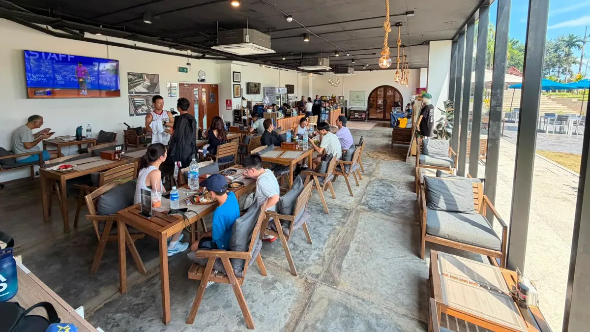 Guests dining at the Courtside Café at KĀHLĪ Phuket, the room opening onto the terrace beside the tennis courts