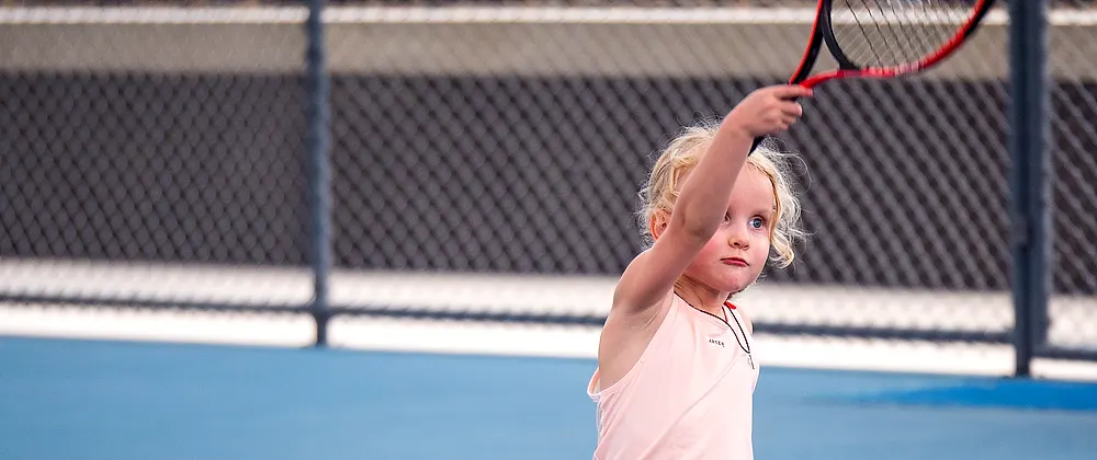 一名小球员在普吉 KĀHLĪ Tennis Academy 的球场上高举球拍准备发球。