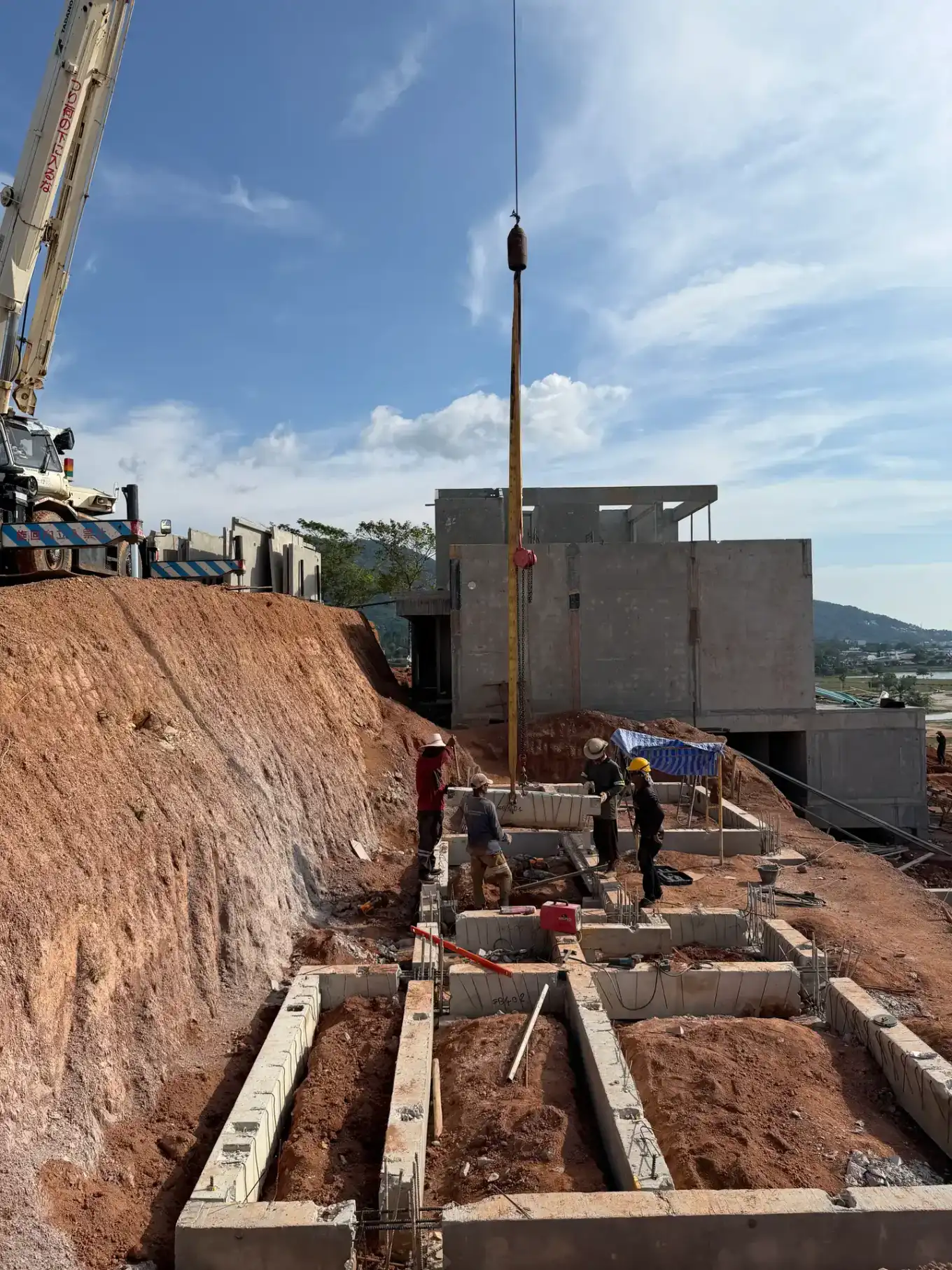 Precast villa structures stepping up the KĀHLĪ Phuket hillside, with a mobile crane on site